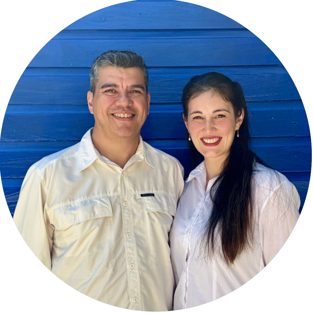Two people smiling in white shirts pose for a photo against a blue wooden wall with planks visible behind them, circular crop shape involved (group portrait).
