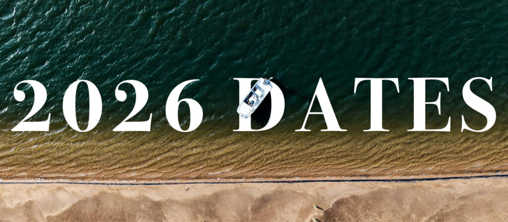 Bold white text reading '2026 DATES' spans a coastal aerial scene with dark sea on top and sandy shore bottom; a small boat rests on the letters.