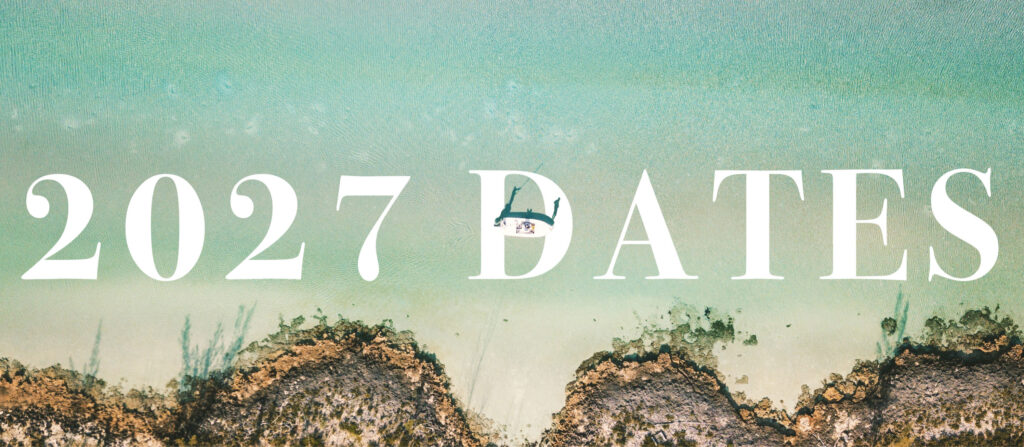 Large white text across a turquoise beach scene reads '2027 DATES'; a small boat sits near the center over the letters with a rocky shoreline at the bottom.